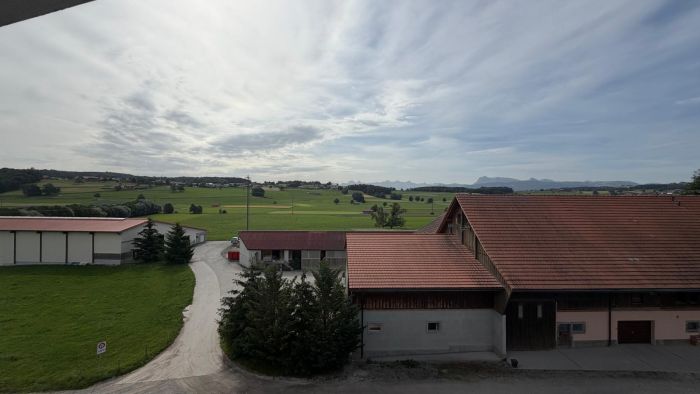 Ländliche Hof- und Alpenlandschaft mit Gebäuden und weitem Ausblick